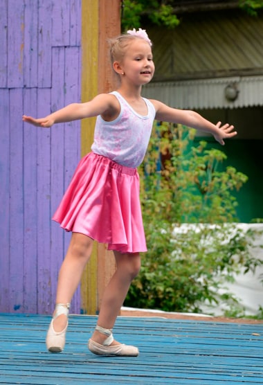 Девочка показывает балетное движение «батман тандю», стоя на сцене «Радужного»