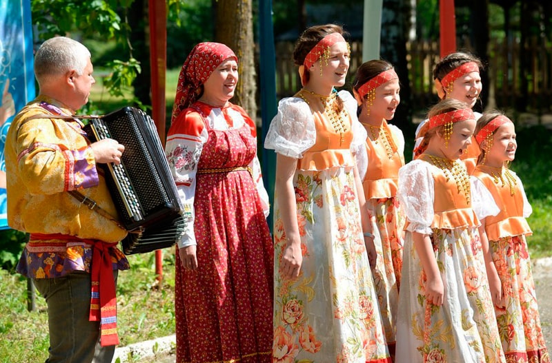Хор поет народные песни под аккордеон. Певцы одеты в народные костюмы. В хоре и взрослые, и дети.